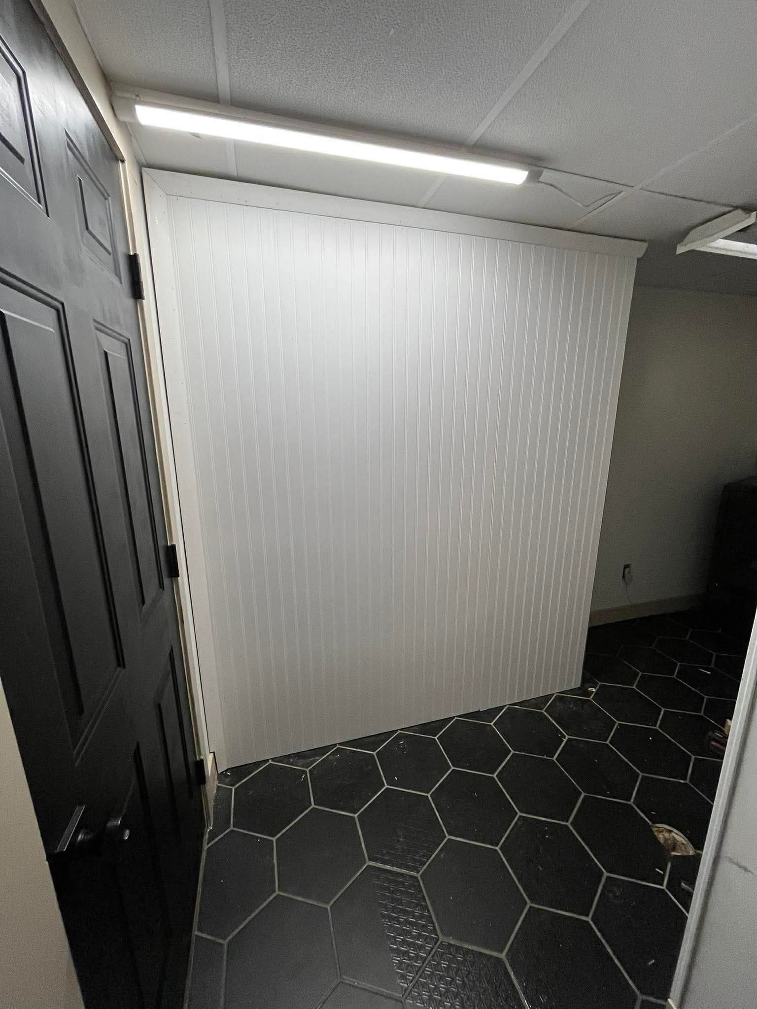 Finished basement with black hexagonal tile flooring, white beadboard walls, and drop ceiling