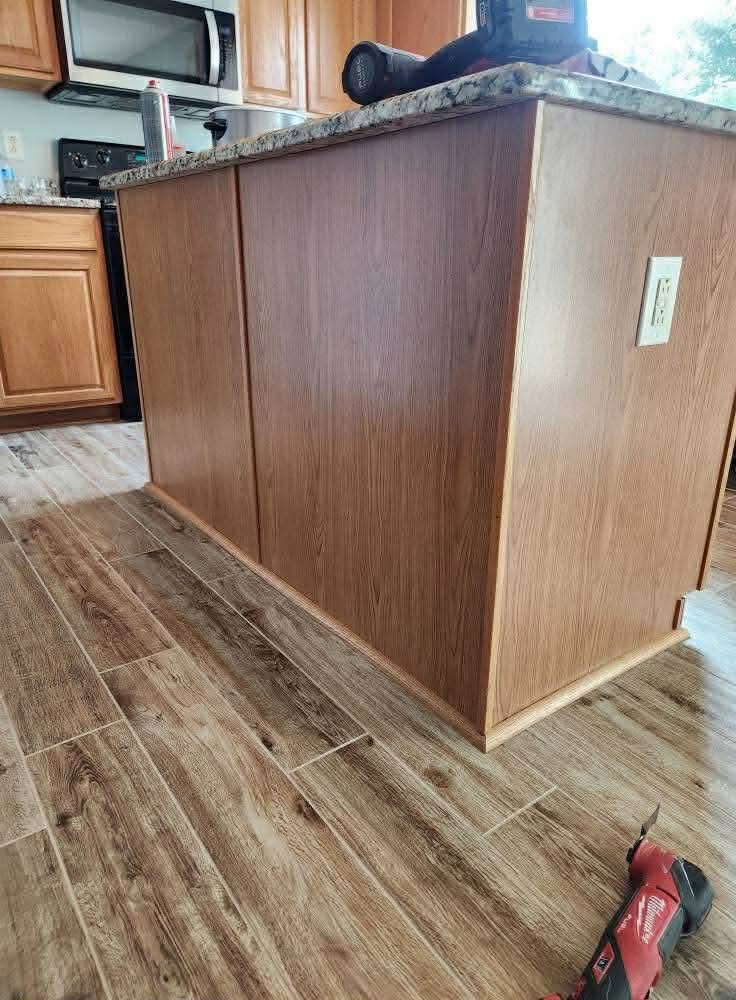 Kitchen island with oak cabinetry, granite countertop, and wood-look tile flooring